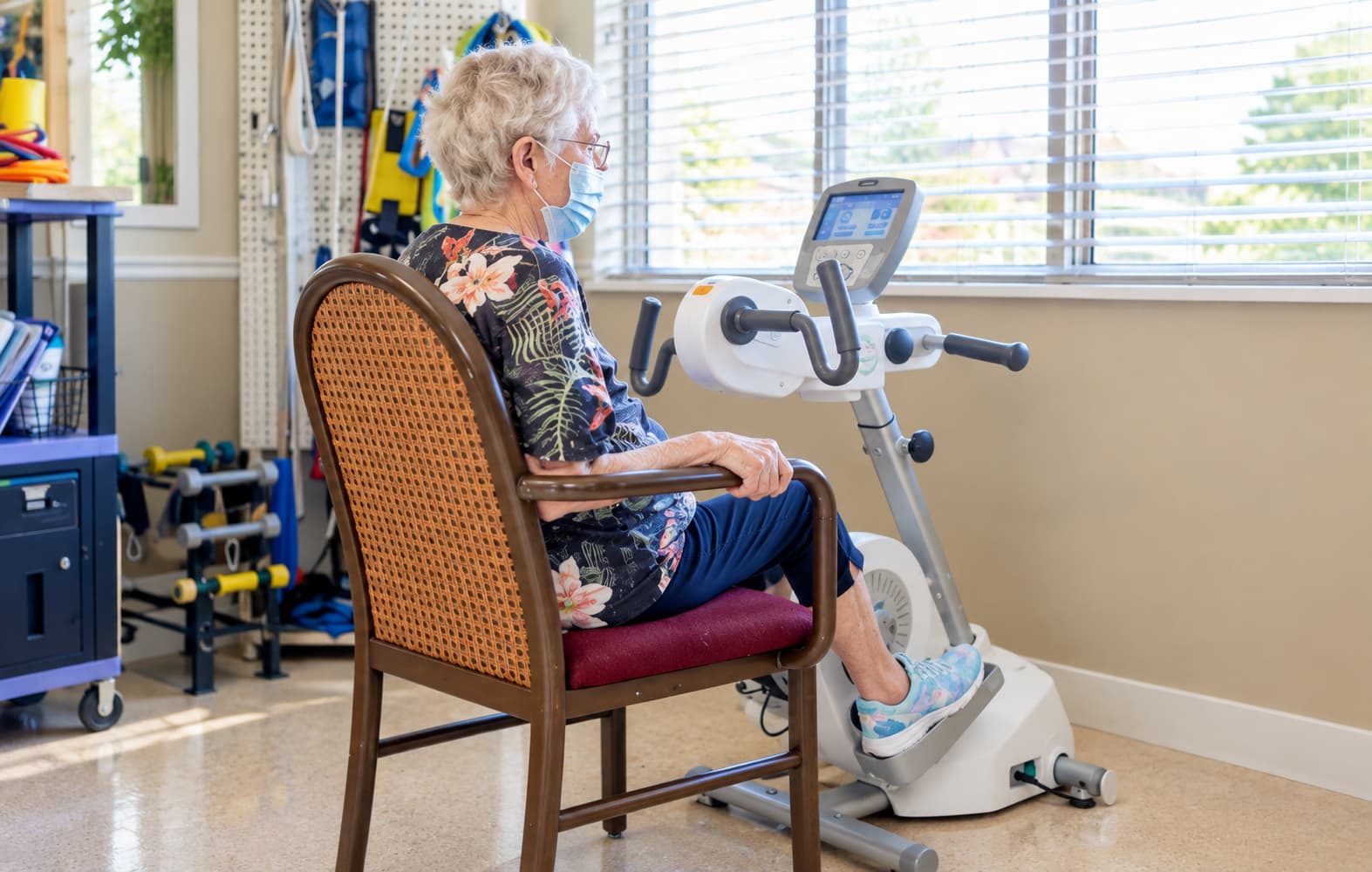 A resident exercising on a pedal trainer while her therapist looks on