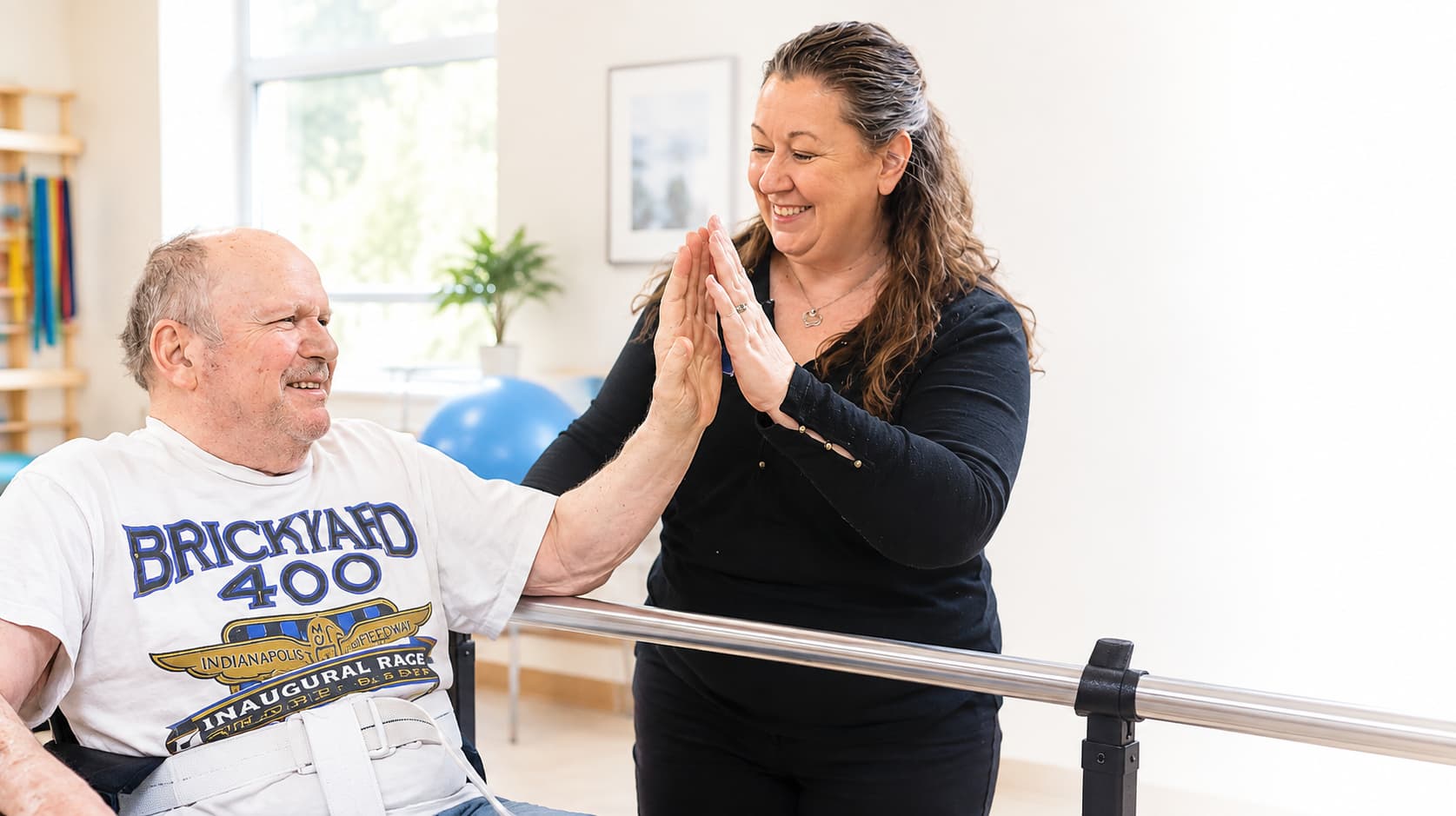 A resident giving his therapist a high five beside the therapy rail