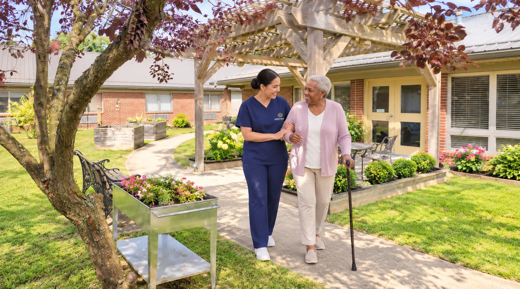 A caregiver walking a resident along a path under blossom