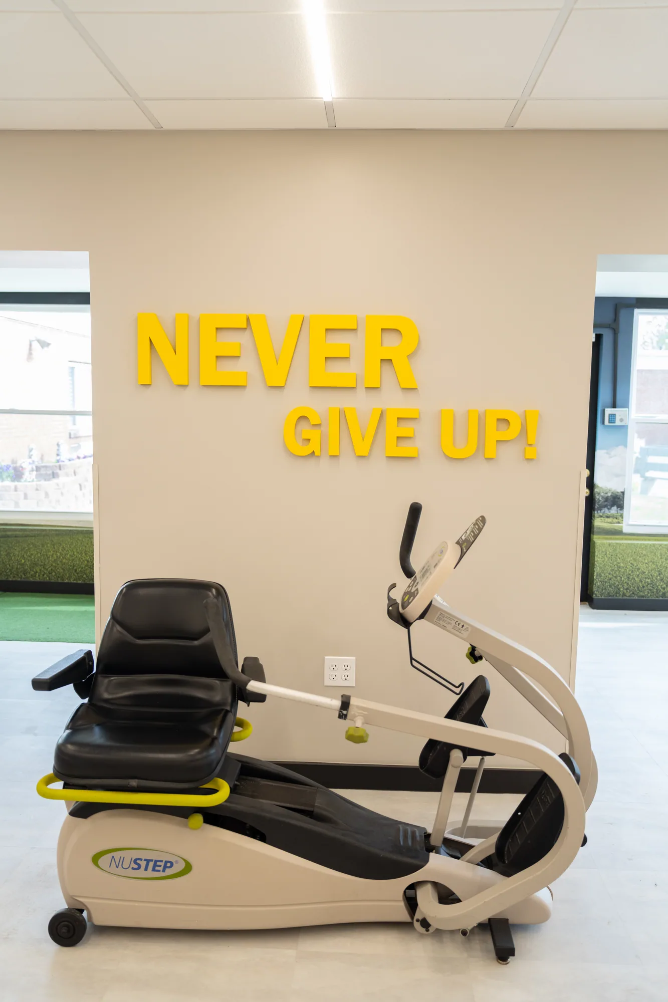 An exercise machine in the therapy gym, below a "Never give up" wall