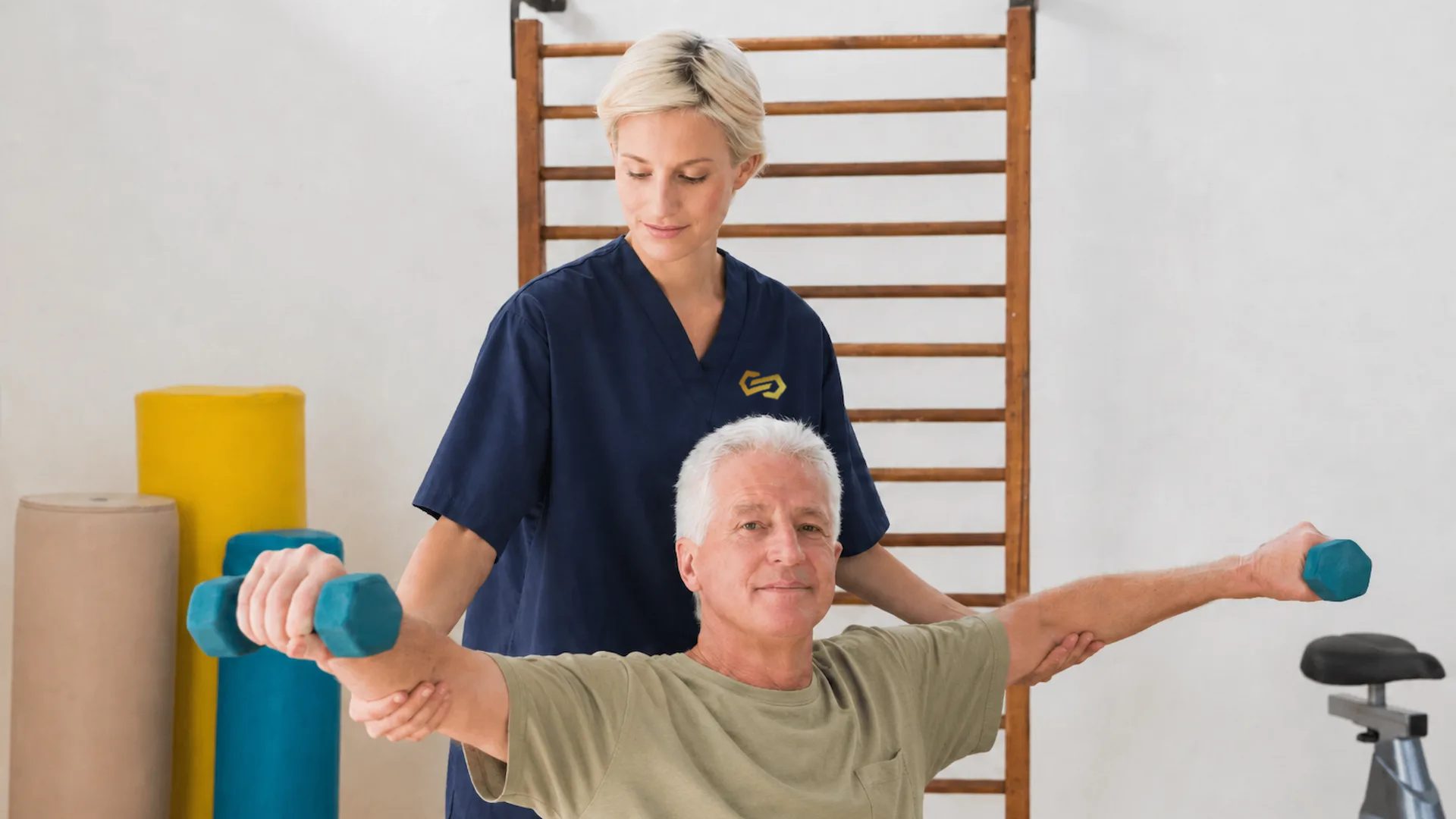 A therapist supports an older man lifting hand weights in the therapy room